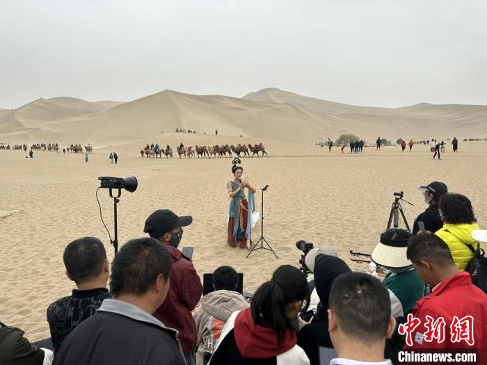 圖為2023年4月底，敦煌大漠“逐舞者”奧楠在鳴沙山月牙泉景區(qū)視頻直播，吸引游人圍觀?！●T志軍 攝